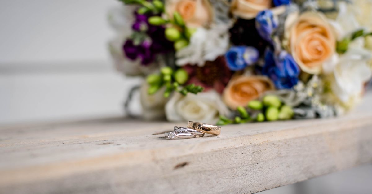 Shiny rings with precious stones near bright blossoming flower bouquet on wooden surface on wedding day